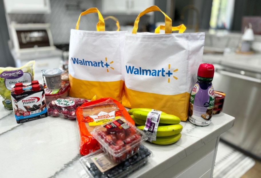walmart plus grocery delivery bags on a kitchen counter with groceries spread around them