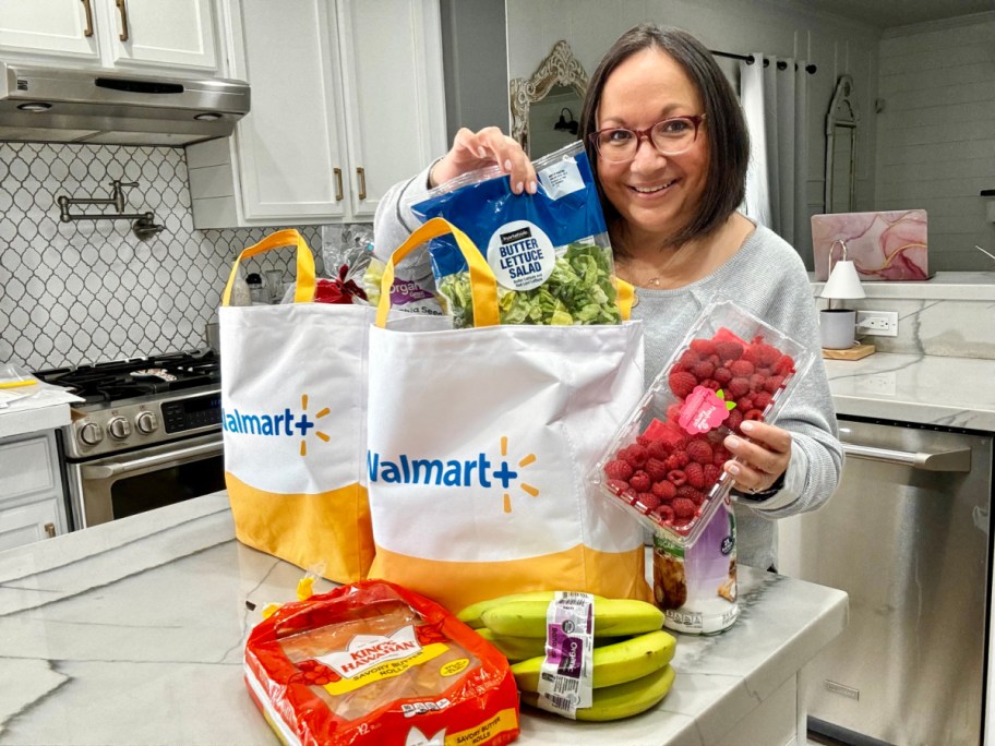 smiling woman with walmart grocery delivery bags and food on her kitchen counter