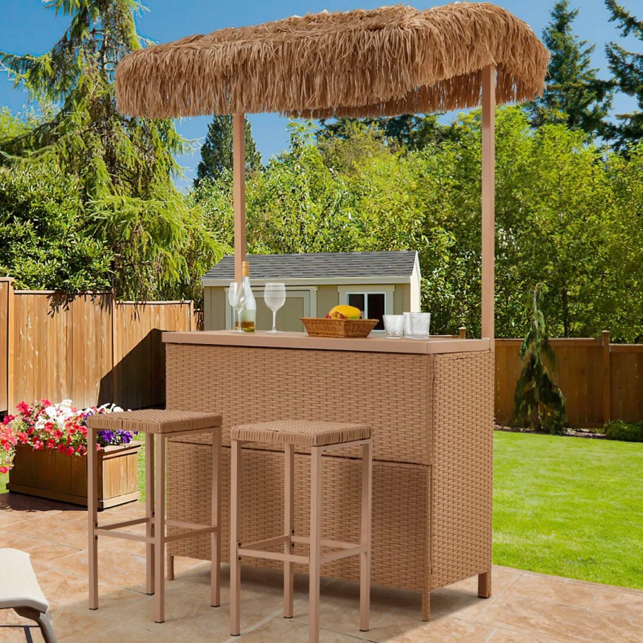 tan tiki bar with chairs in front of it in backyard