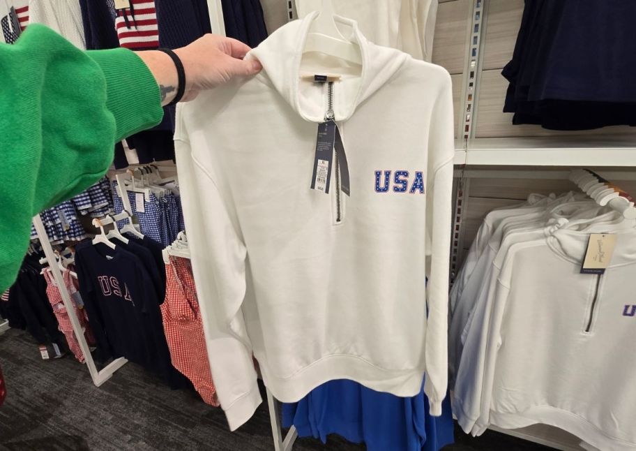 a womans hand holding out a white half zip sweatshirt