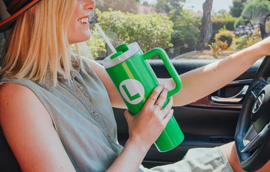 a woman behind the wheel of a car drinking from a green tumbler