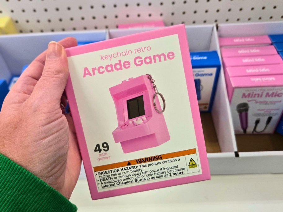 hand holding a box with a mini arcade game keychain, more on a store shelf behind it