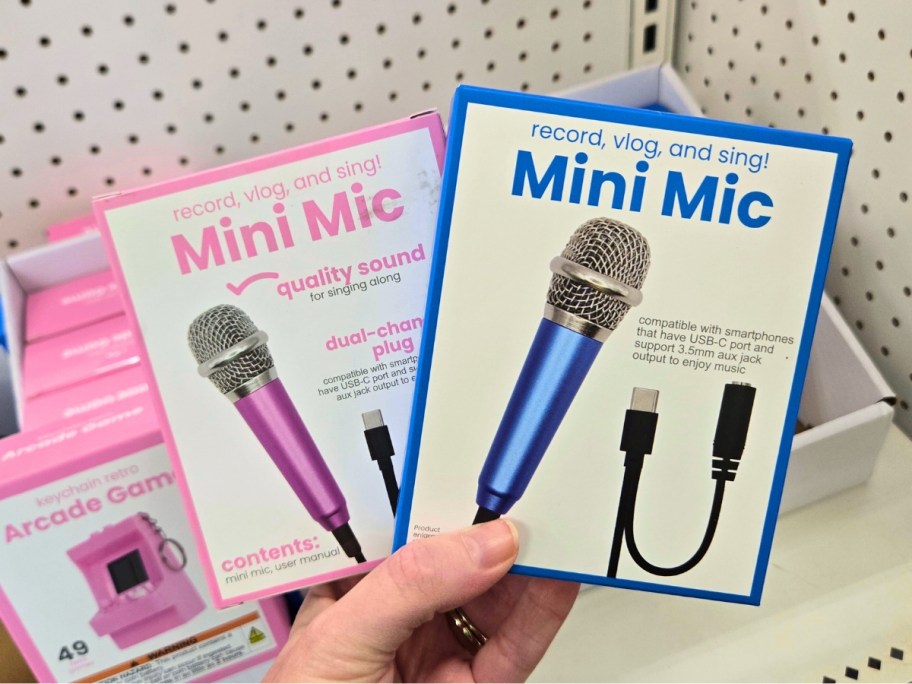 hand holding 2 boxes with mini microphones, more on a store shelf behind them