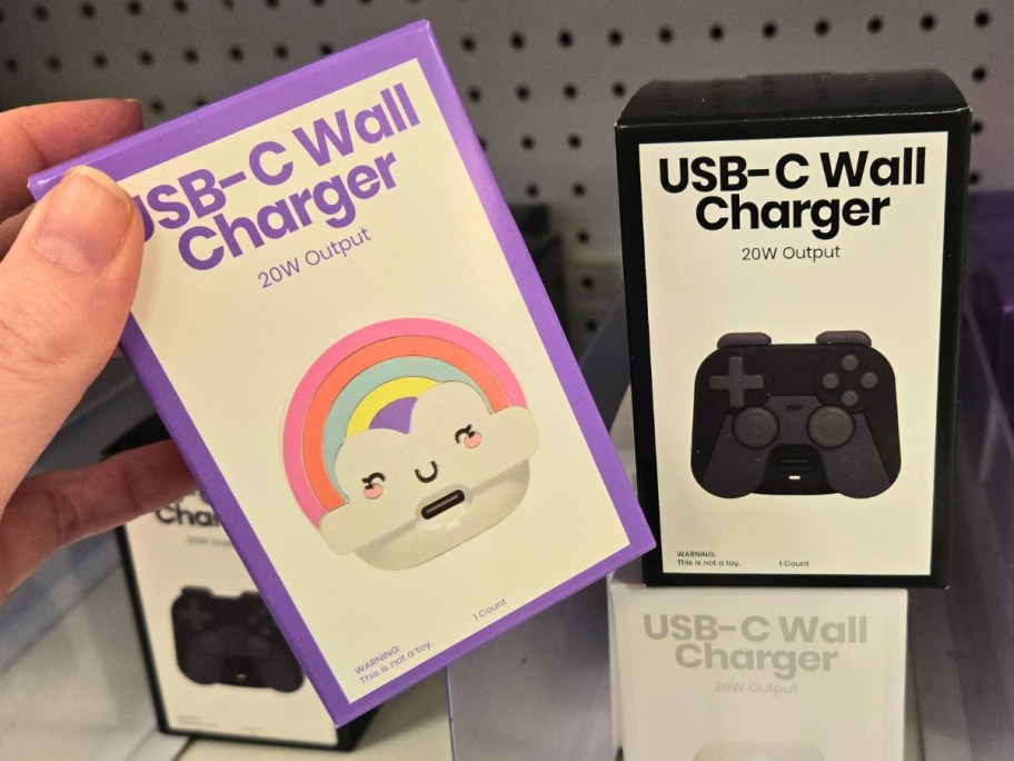 hand holding a box with a USB wall charger, more on a store shelf behind it